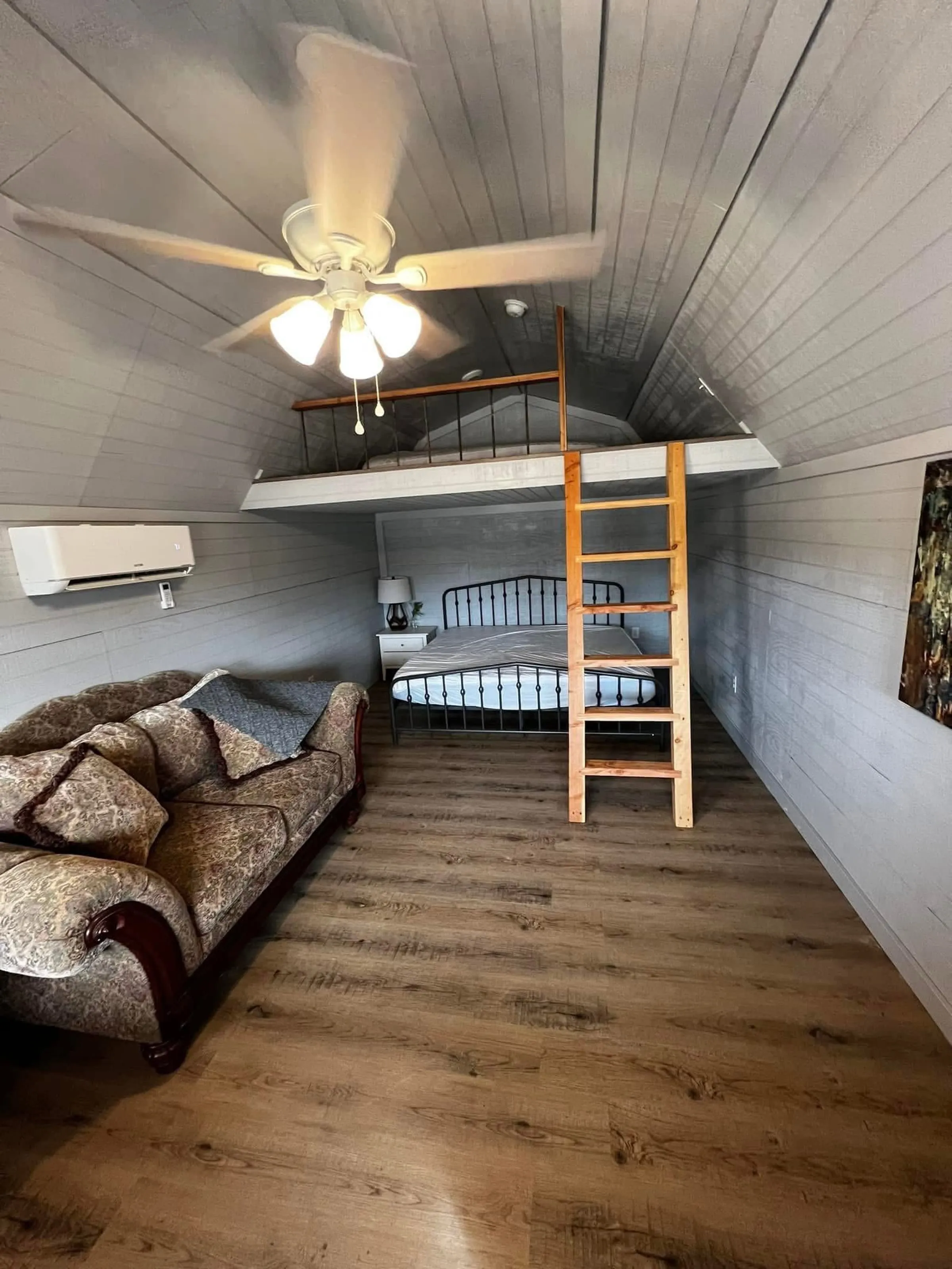 A cozy cabin interior with a queen bed, sleeping loft, and sitting area