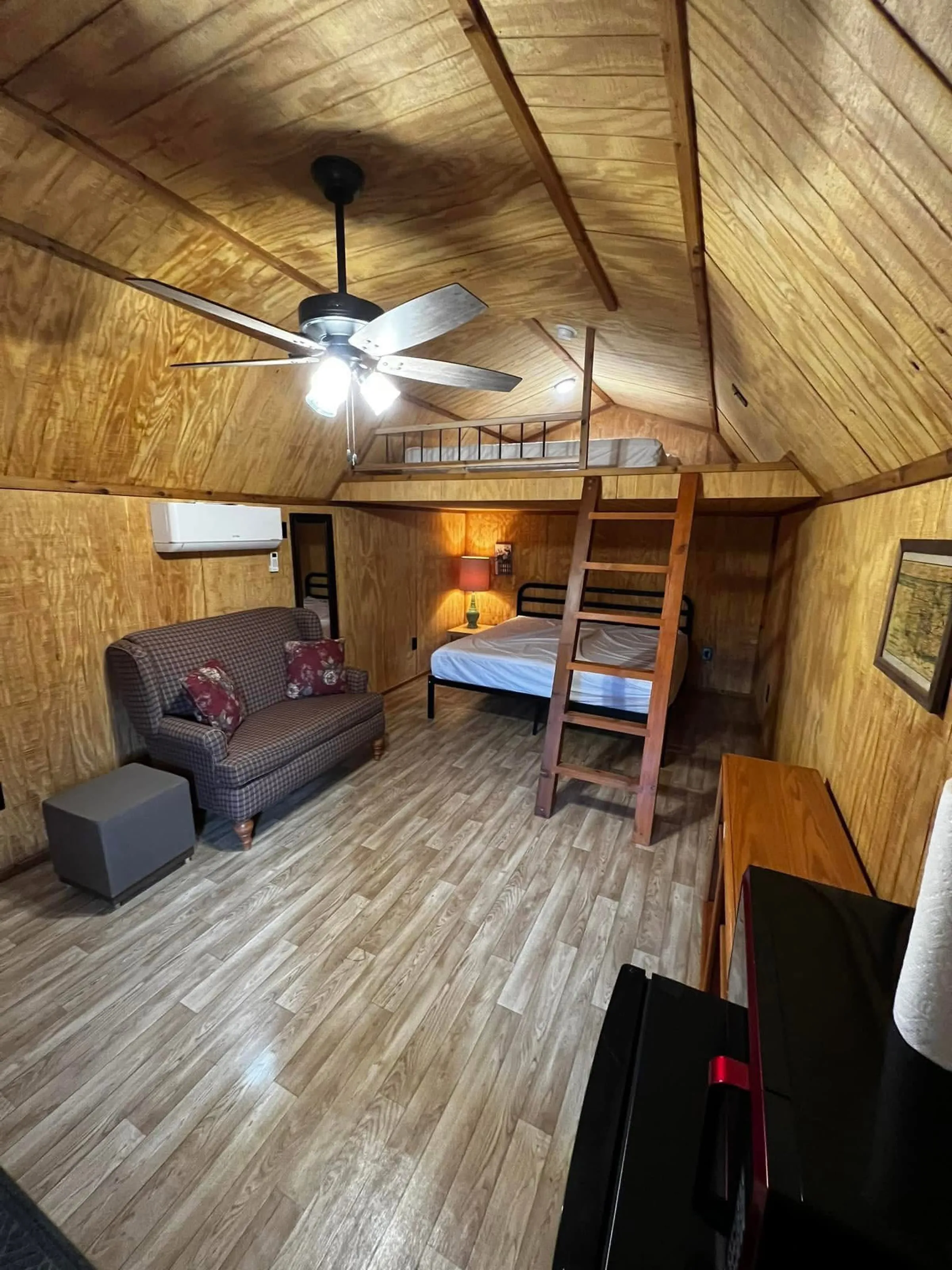 A wood-paneled cabin interior with a loft bed and sitting area