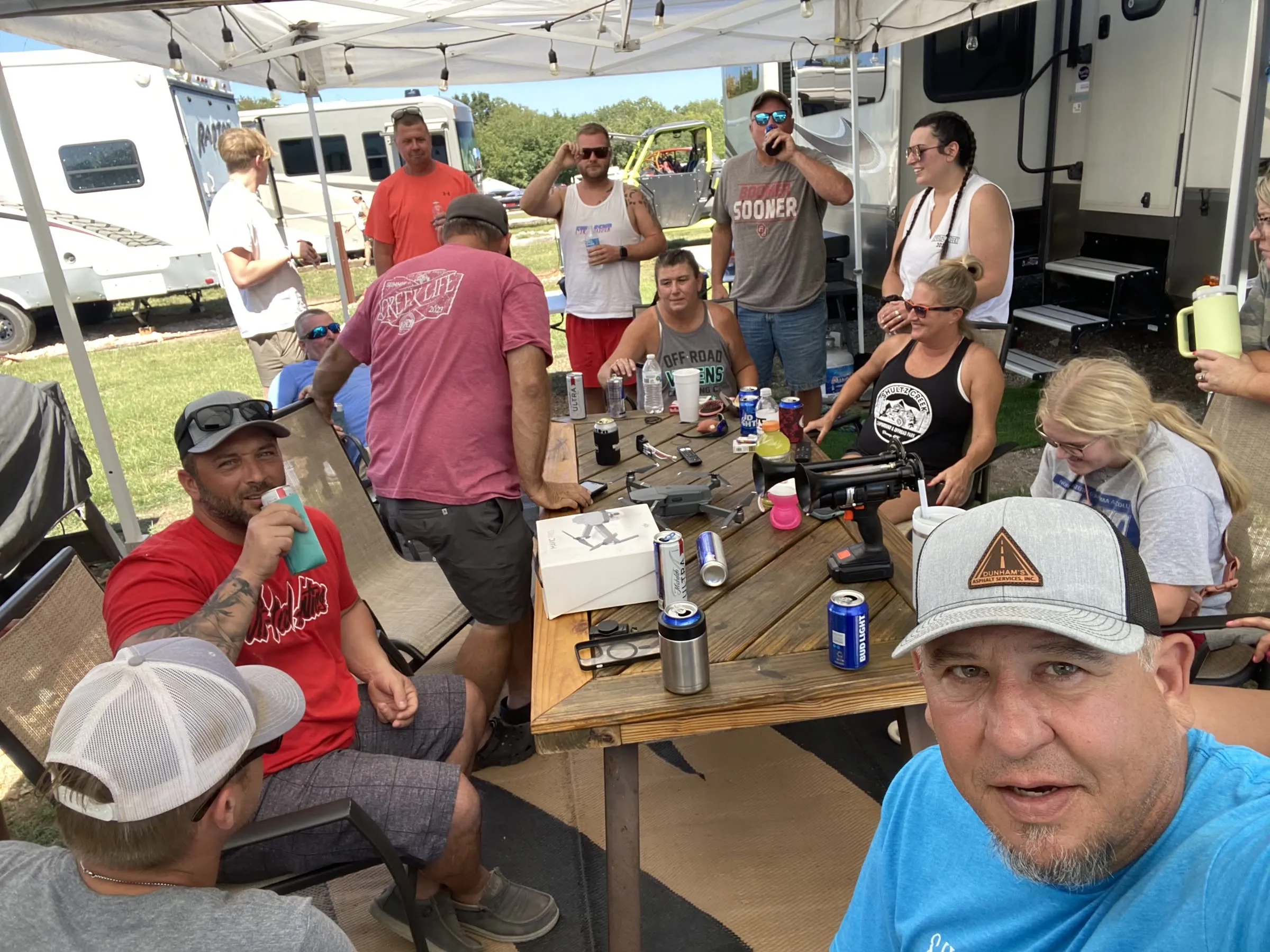 A group of campers gathered under a canopy at a picnic table