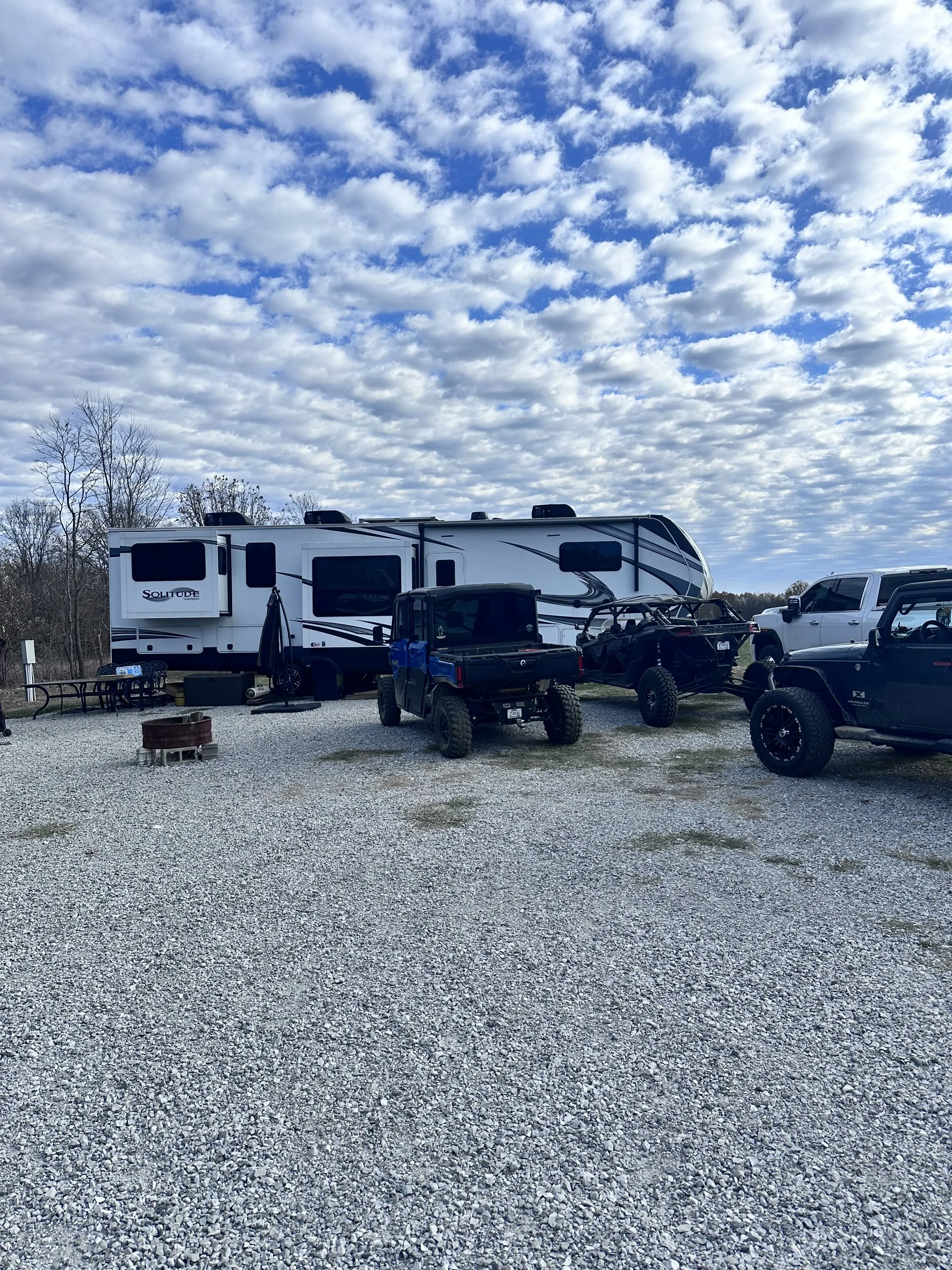 An RV site with a fire pit, picnic table, and UTVs parked alongside