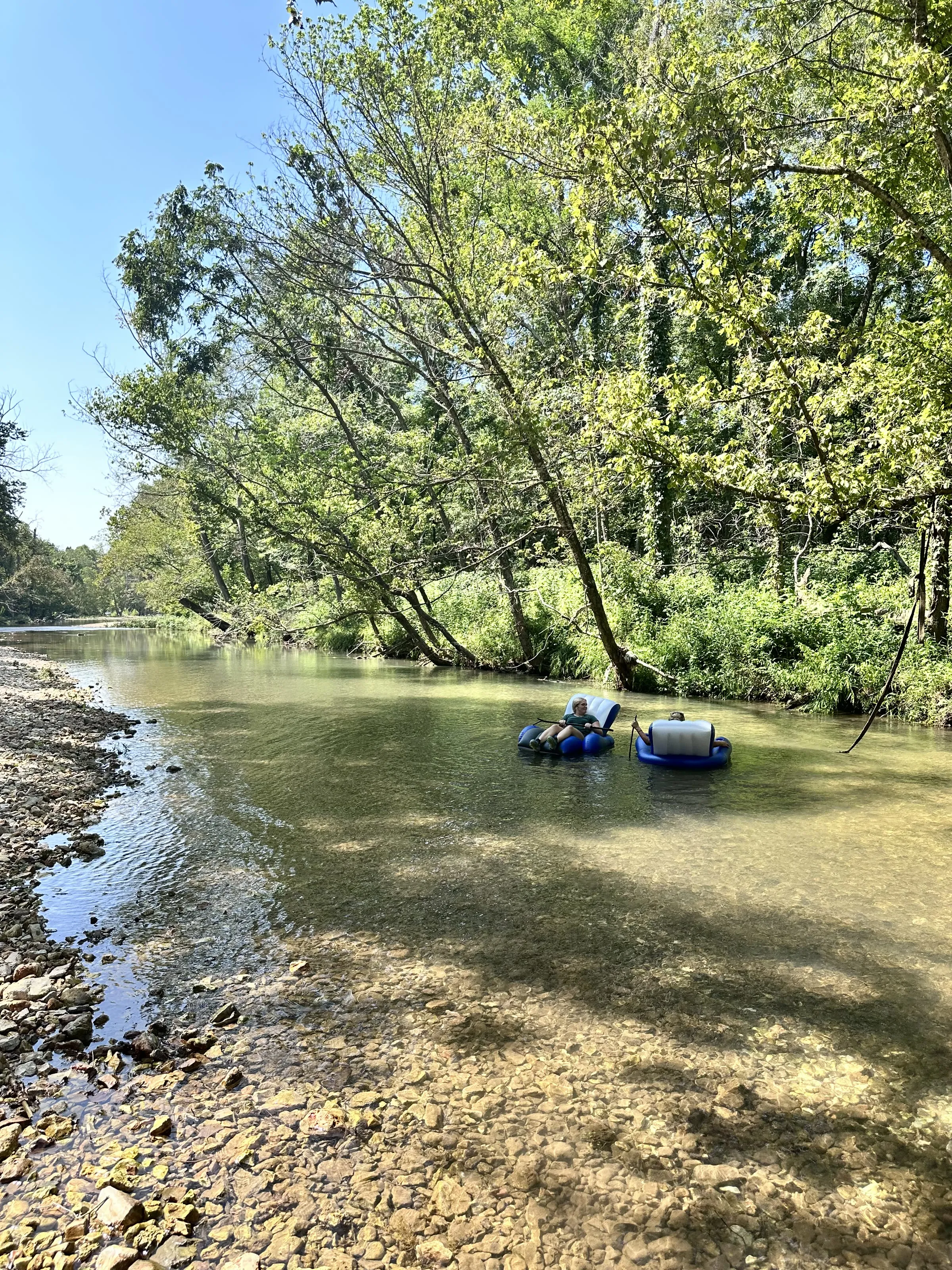 Two riders relaxing on inflatable loungers in a calm, clear stretch of Shultz Creek