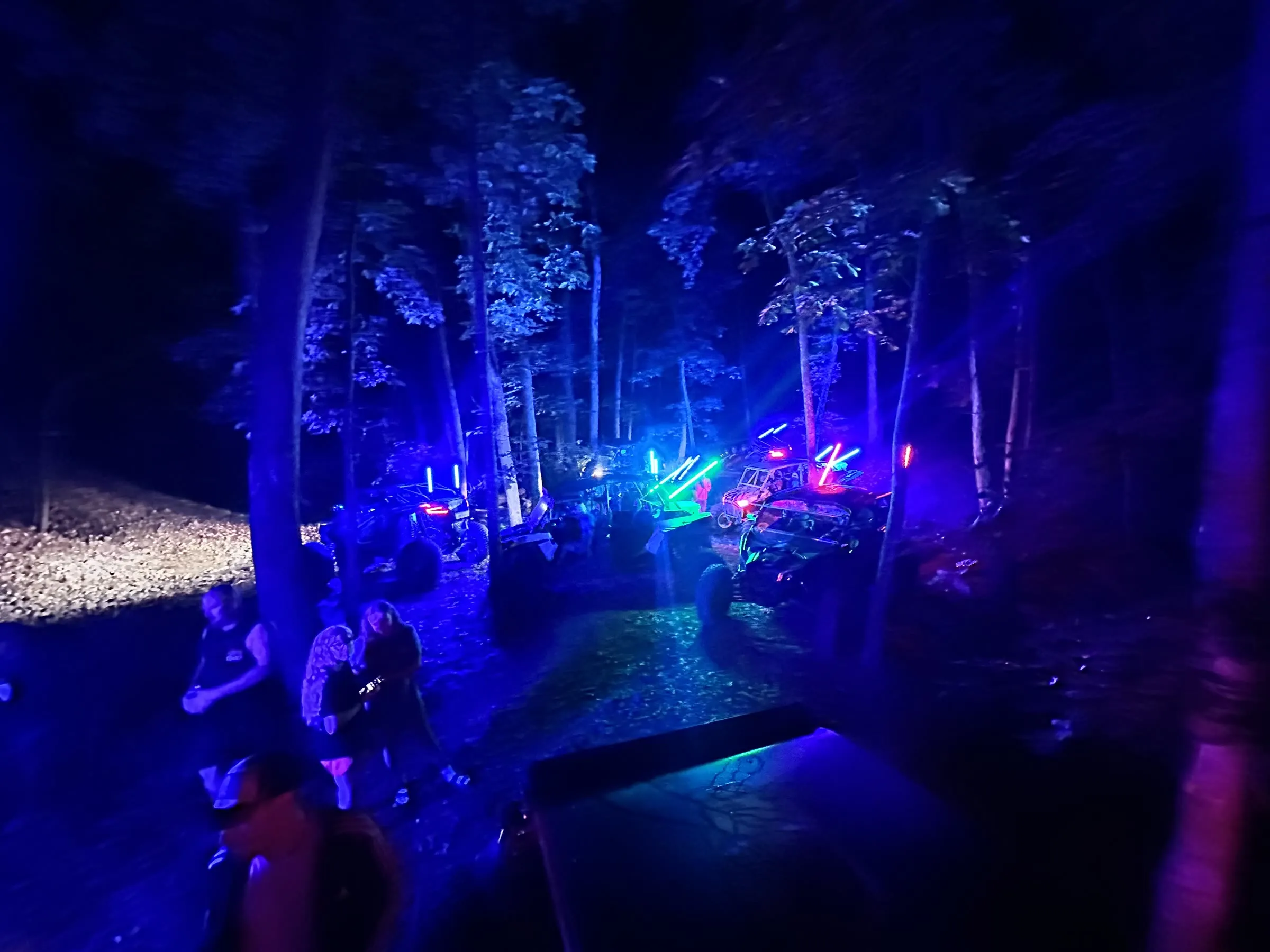 UTVs with colorful LED whip lights gathered in the woods at night