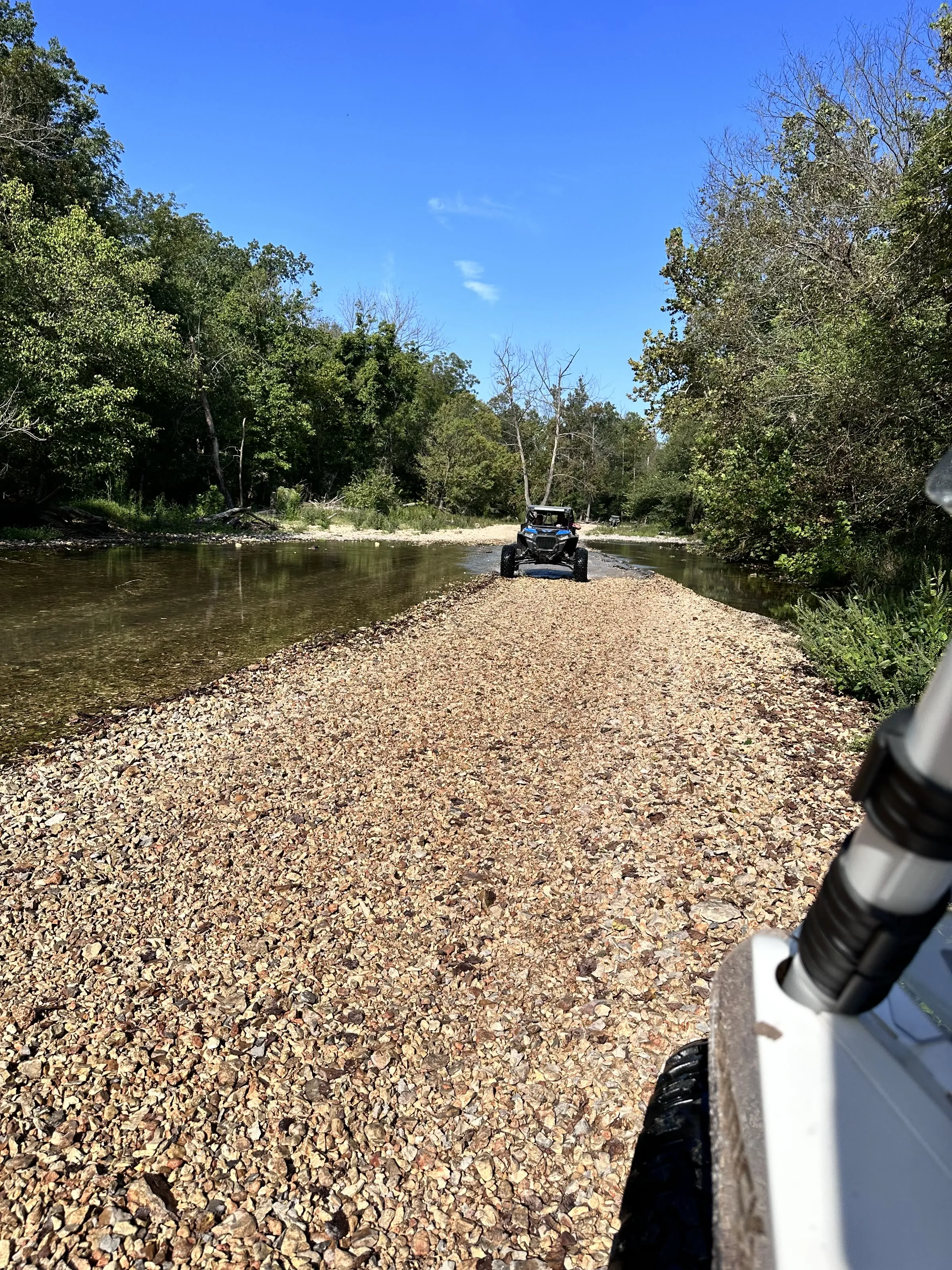 Point-of-view shot riding down a gravel-bar trail behind another UTV