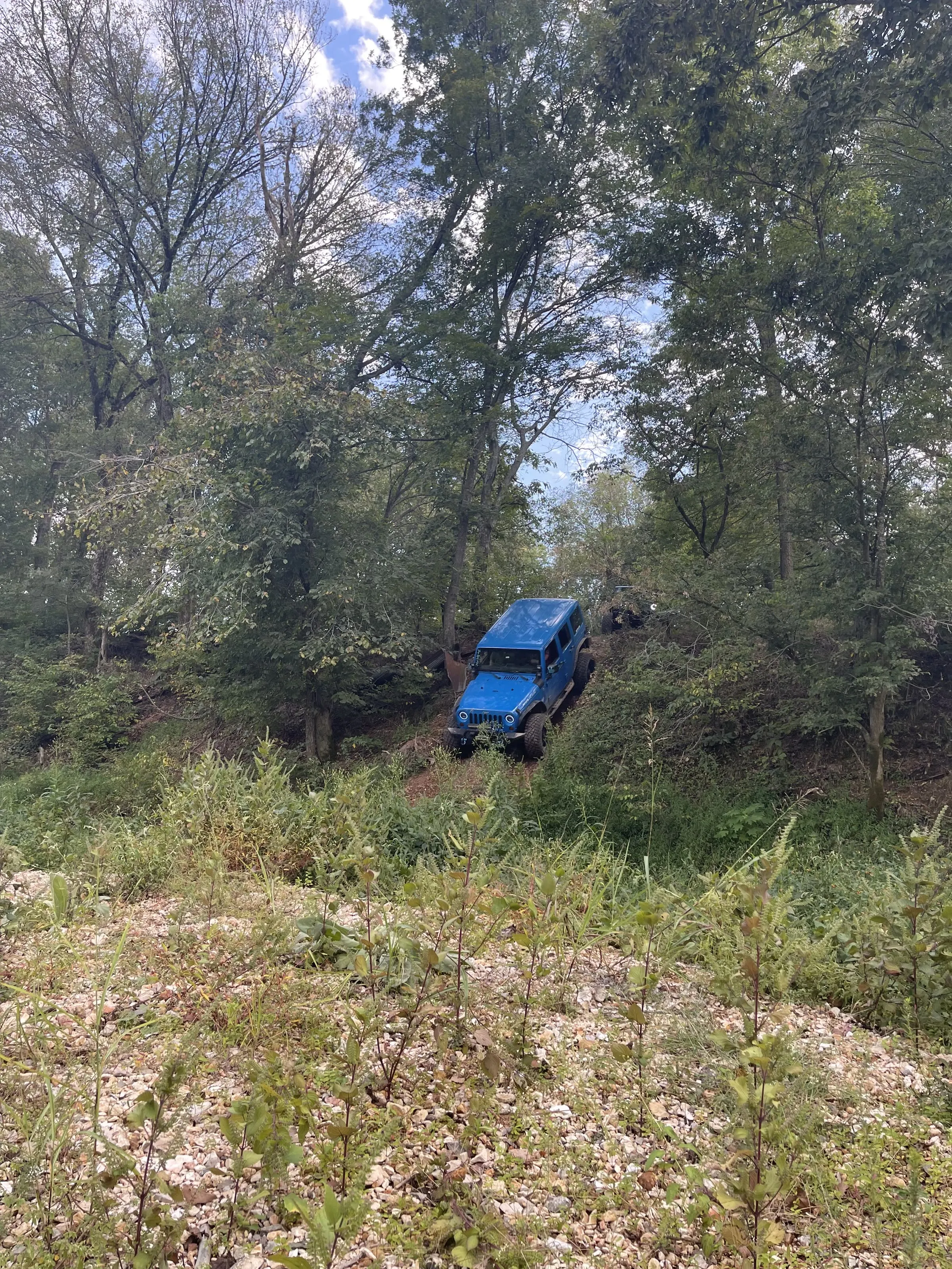 A blue Jeep climbing a steep, wooded hillside trail