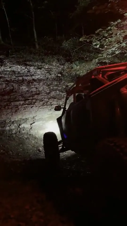A UTV with red lights approaching down a muddy night trail